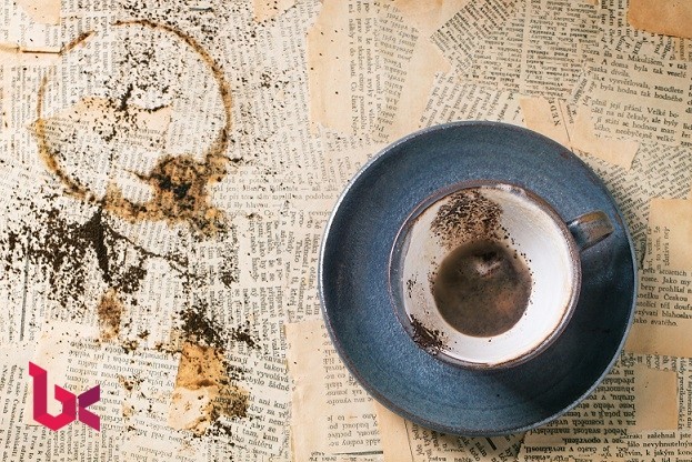 Blue ceramic cup of coffee grounds over old newspaper. Top view.